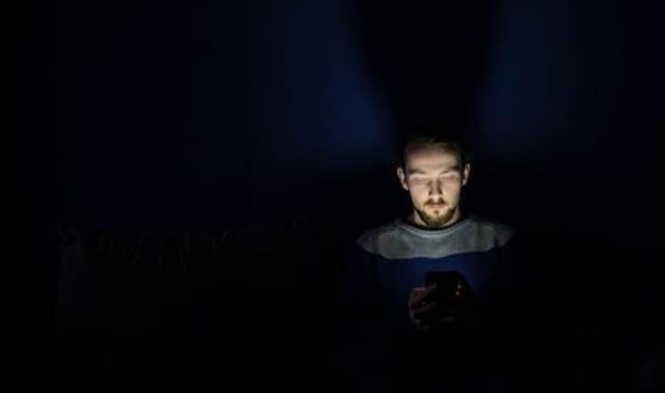 homem no escuro iluminado pelo celular