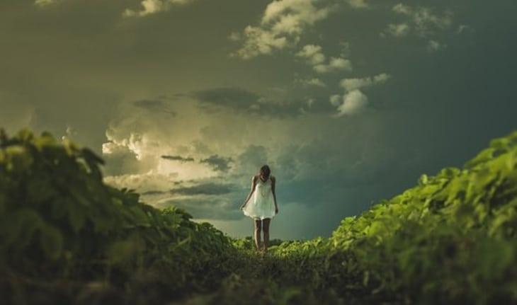 mulher longe no mato com céu nublado ao fundo