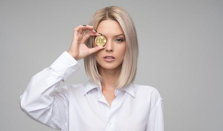 mulher branca segurando moeda na frente do olho